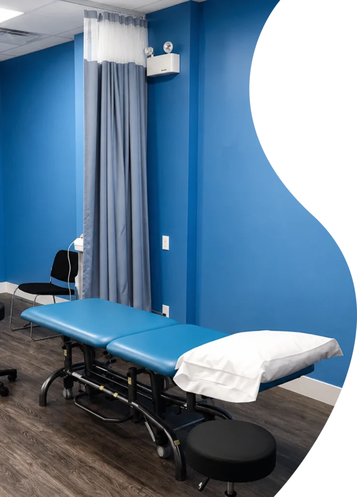 An empty treatment room featuring a blue adjustable therapy table, privacy curtain, and stool ready for patient care.