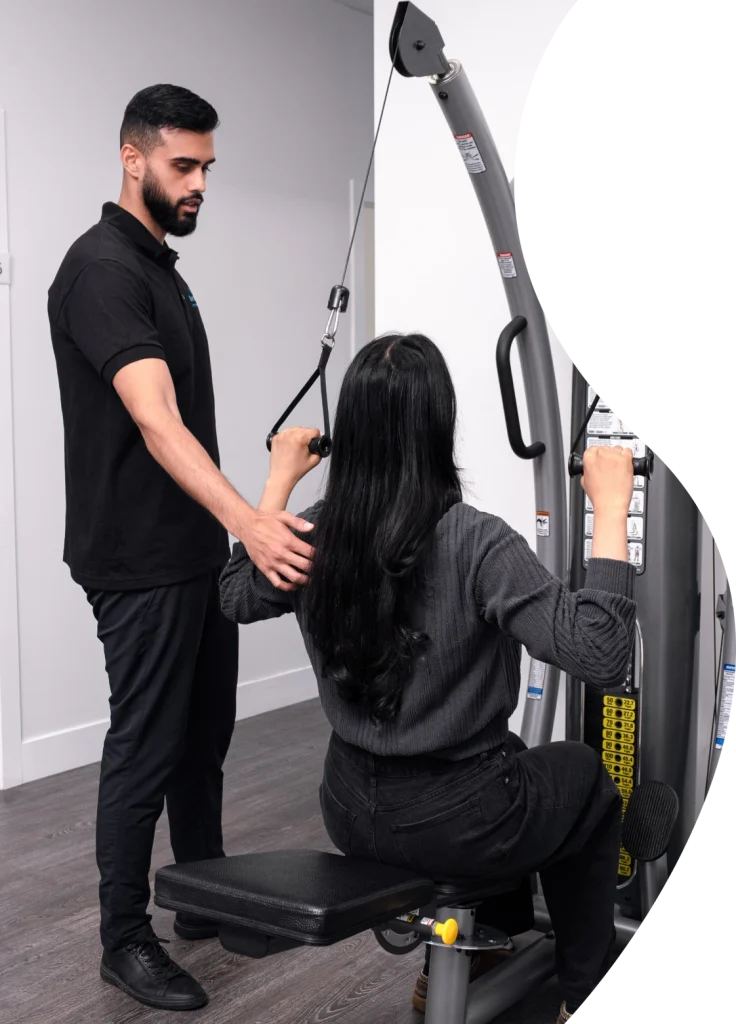 A Smart Motion Physiotherapy kinesiologist supports a patient during an active strengthening exercise on a cable machine.